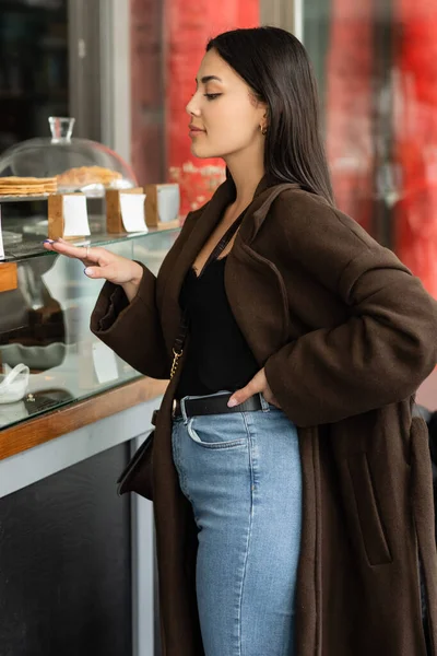 Vue latérale de la femme brune branchée touchant vitrine de la pâtisserie boutique à prague — Photo de stock