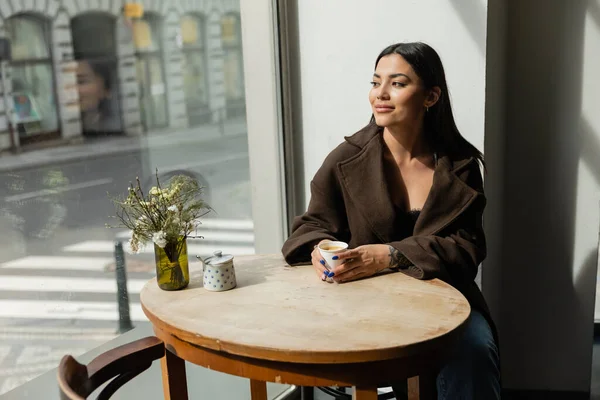 Happy woman looking at urban street while sitting near window in cafe in prague — Stock Photo