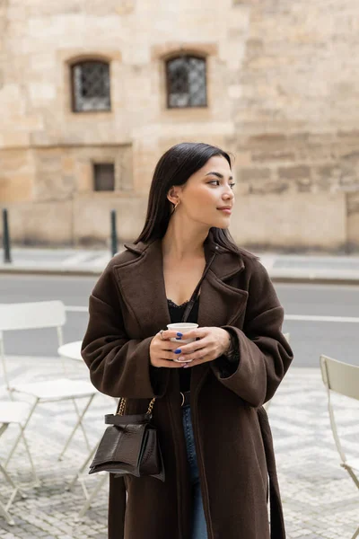 Молодая женщина в пальто держит бумажную чашку на городской улице в Праге — стоковое фото