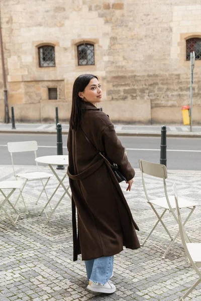 Stylish woman in coat walking near chair of outdoor cafe in Prague — Stock Photo