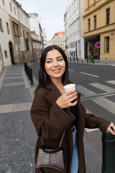Portrait of stylish young woman holding paper cup with coffee on blurred street in Prague — Stock Photo