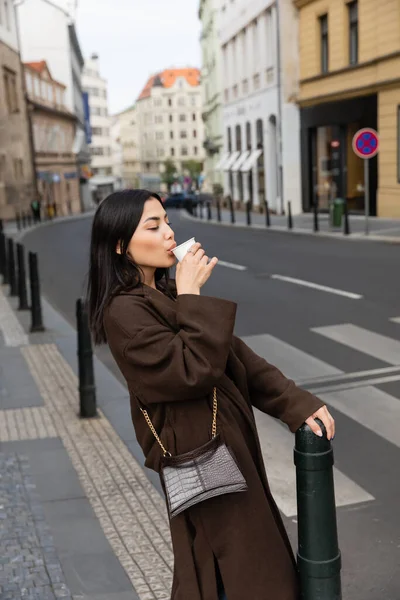 Mulher elegante no casaco beber café de xícara de papel na rua urbana em Praga — Fotografia de Stock