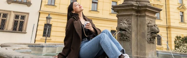Zufriedene Frau im Mantel mit Pappbecher in der Nähe des Brunnens auf dem Karlsplatz in Prag, Banner — Stockfoto