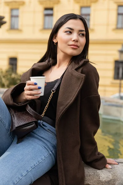 Portrait of stylish traveler holding paper cup near blurred fountain in Prague — Stock Photo