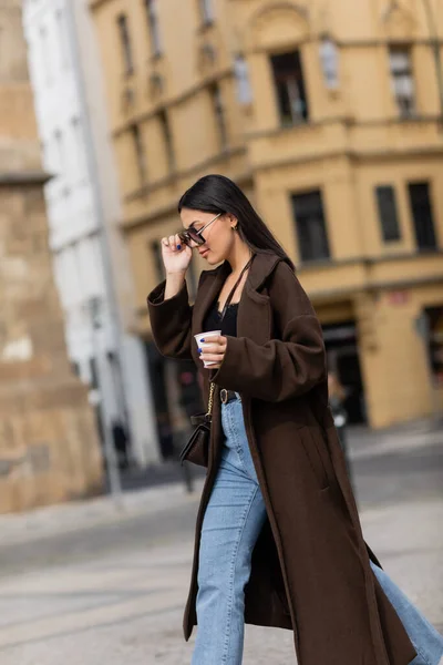 Seitenansicht eines stilvollen Touristen in Mantel und Sonnenbrille mit Kaffee zum Mitnehmen auf der Straße in Prag — Stockfoto