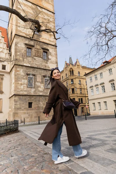 Glücklicher junger Tourist in Sonnenbrille und Mantel schaut auf der Straße in Prag weg — Stockfoto