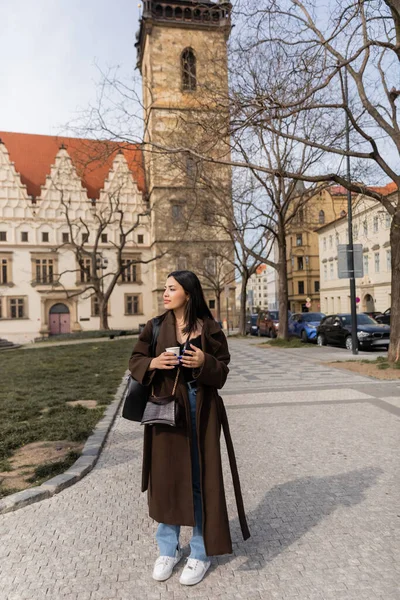Модная молодая женщина в пальто держит кофе, чтобы пойти на городской улице в Праге — стоковое фото