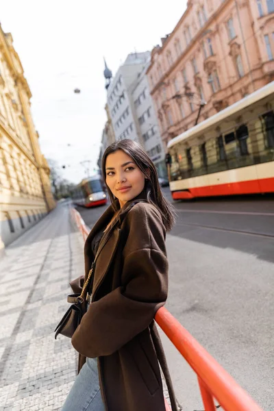 Femme souriante en manteau regardant la caméra dans la rue urbaine de Prague — Photo de stock