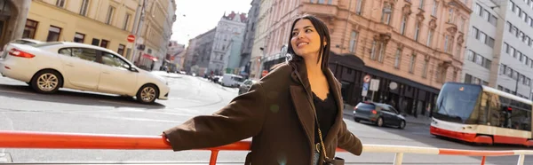 Happy brunette woman standing near road railing on urban street in Prague, banner — Stock Photo