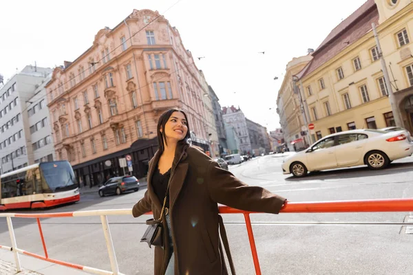 Усміхнена жінка в пальто, яка дивиться на залізницю і дорогу на вулиці в Празі. — Stock Photo