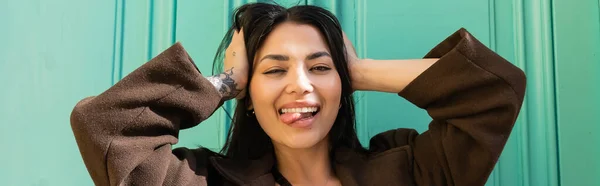 Femme tatouée en manteau collant la langue et regardant la caméra sur la rue, bannière — Photo de stock