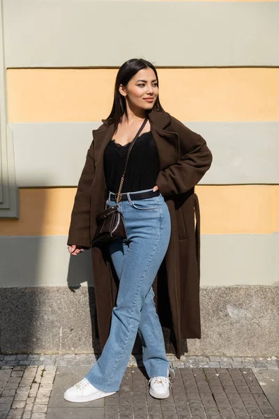 Trendige Frau im Mantel hält Hand an Hüfte auf urbaner Straße — Stockfoto