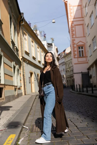 Comprimento total de mulher elegante no casaco andando na estrada entre edifícios na rua em Praga — Fotografia de Stock