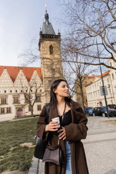 Турист з паперовою чашкою йде по міській вулиці і озирається назад у Празі. — стокове фото