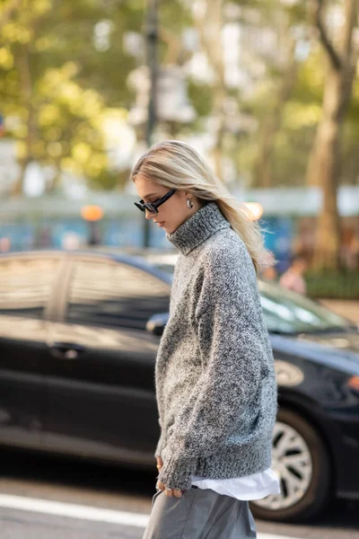 Femme à la mode en pull gris et lunettes de soleil marchant sur la rue de New York — Photo de stock