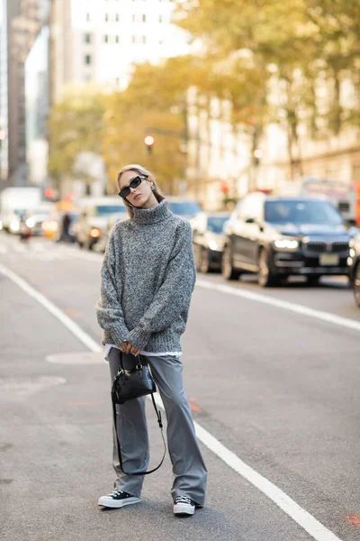 Comprimento total da mulher elegante em óculos de sol e roupa cinza segurando bolsa preta na rua da cidade de Nova York — Fotografia de Stock