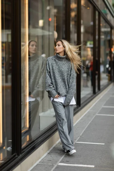 Comprimento total de mulher jovem e elegante em roupa cinza em pé perto de vitrine em Nova York — Fotografia de Stock