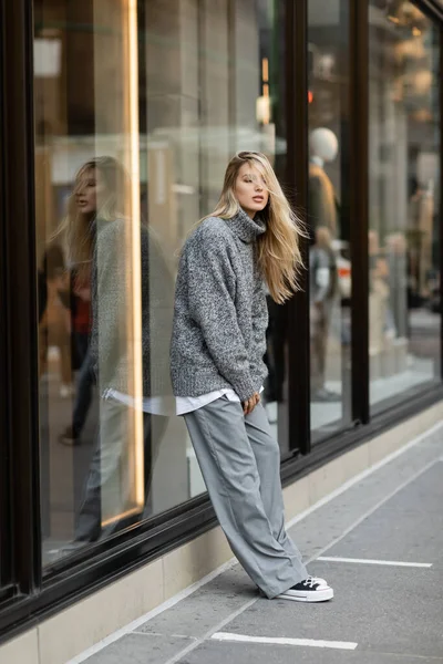 Full length of young woman in stylish winter outfit standing near window display in New York — Stock Photo