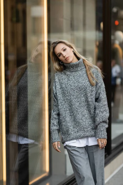 Mujer joven en traje gris apoyada en la pantalla de la ventana en Nueva York - foto de stock