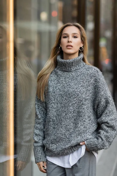 Jovem mulher em roupa de inverno em pé com a mão no bolso perto de vitrine em Nova York — Fotografia de Stock
