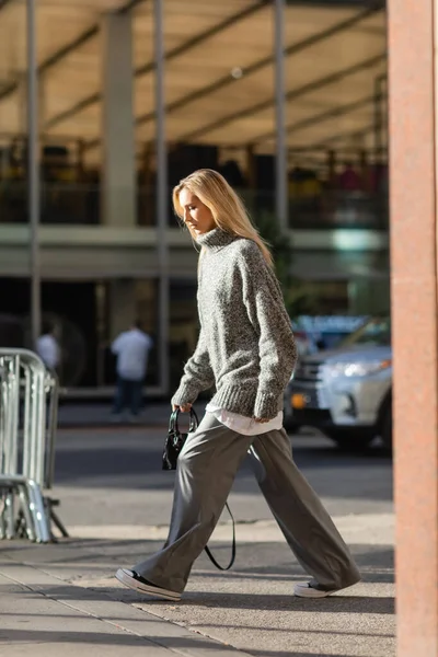 Pleine longueur de jeune femme élégante avec des cheveux blonds marchant dans une tenue d'hiver à la mode à New York — Photo de stock