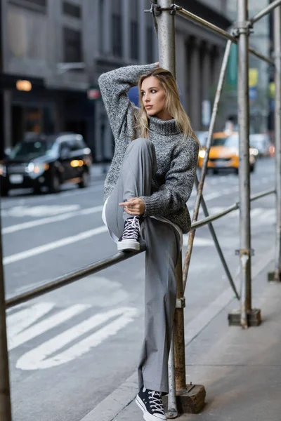 Full length of stylish young woman in trendy winter outfit sitting on urban street in New York — Stock Photo