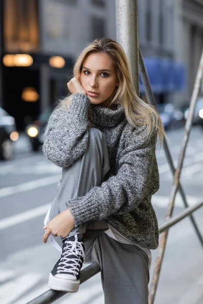 Young blonde woman in trendy winter outfit and footwear sitting on urban street in New York — Stock Photo
