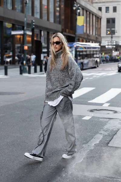 Довга блондинка в стильному в'язаному светрі і сонцезахисні окуляри йдуть по міській вулиці в Нью-Йорку. — стокове фото