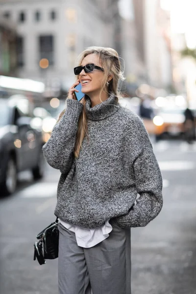 Mulher feliz em camisola de inverno e óculos de sol falando no smartphone na cidade de Nova York — Fotografia de Stock