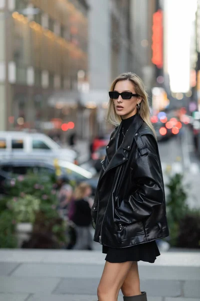 Mulher elegante em jaqueta de couro e vestido preto de pé com a mão no bolso em Nova York — Fotografia de Stock
