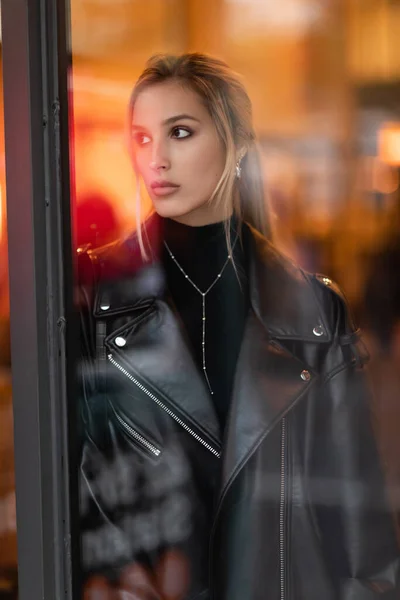 Mulher loira em jaqueta de couro preto olhando através da janela de vidro em Nova York — Fotografia de Stock