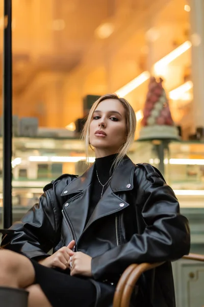 Junge blonde Frau in schwarzer Lederjacke sitzt in der Nähe eines Cafés in New York — Stockfoto