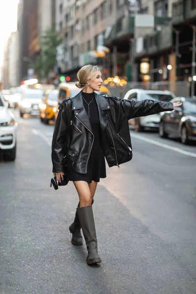 Comprimento total da mulher loira em jaqueta de couro preto e vestido de captura de táxi na rua em Nova York — Fotografia de Stock
