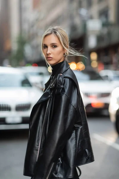 Retrato de mulher loira em jaqueta de couro elegante olhando para a câmera na rua urbana em Nova York — Fotografia de Stock