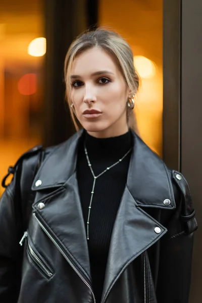 Portrait de jeune femme blonde veste en cuir noir regardant caméra à l'extérieur — Photo de stock