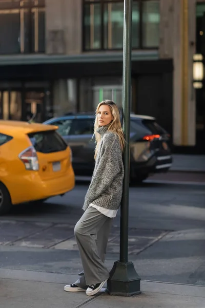 Полная длина стильной молодой женщины в вязаном зимнем свитере, стоящей возле уличного столба в Нью-Йорке — стоковое фото