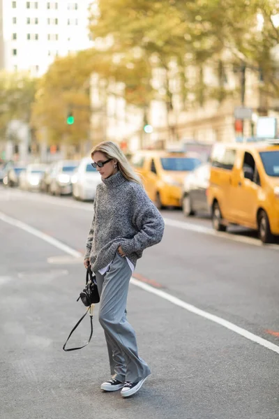 Full length of pretty young woman in winter outfit walking with trendy handbag near blurred cars in New York — Stock Photo