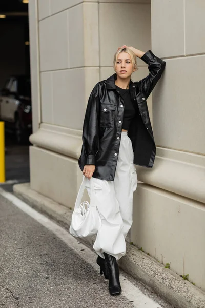 Comprimento total de mulher loira em roupa elegante e botas posando com bolsa na rua em Miami — Fotografia de Stock