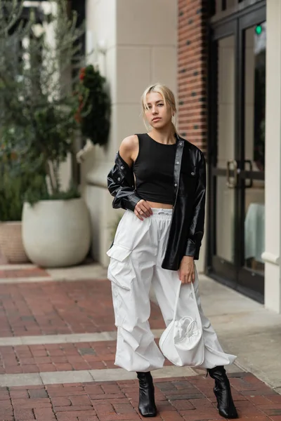 Junge blonde Frau in Lederjacke posiert mit Handtasche auf Straße in Miami — Stockfoto