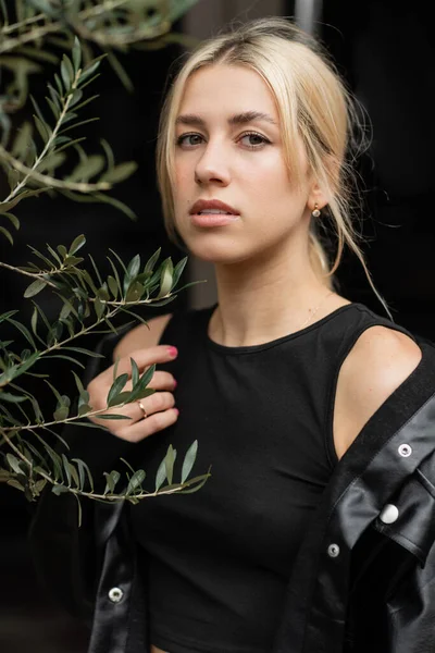 Portrait of blonde woman in leather shirt jacket standing near plant — Stock Photo