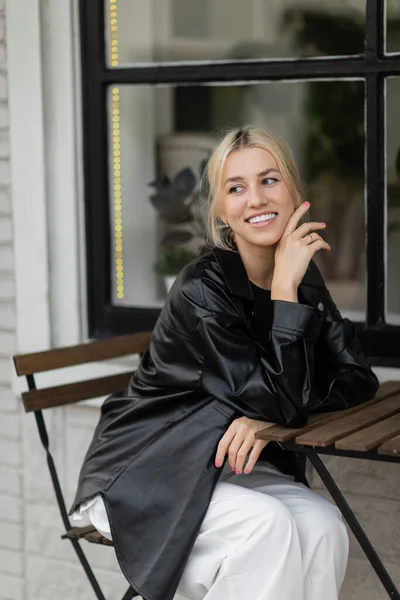 Joyful young woman in leather shirt jacket sitting in outdoor cafe on street in Miami — Stock Photo
