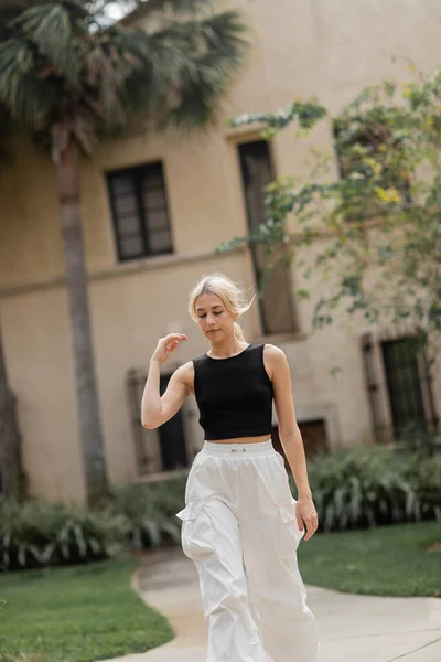 Young woman in white cargo pants and trendy tank top walking near house in Miami — Stock Photo