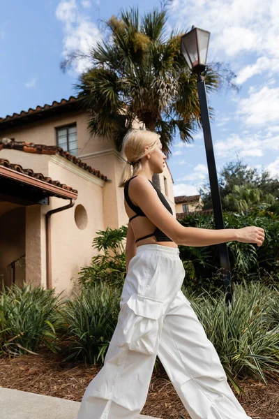 Vista laterale di giovane donna in abiti alla moda a piedi vicino alla casa moderna a Miami — Foto stock