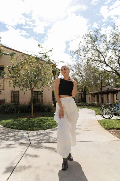Piena lunghezza della donna positiva in abiti alla moda in piedi in stivali alla moda vicino alla casa moderna a Miami — Foto stock