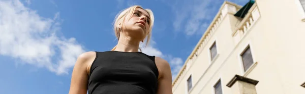 Low angle view of blonde woman in tank top standing near building in Miami, banner — Stock Photo