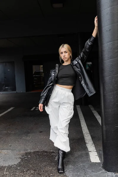 Pleine longueur de jeune femme blonde en veste chemise en cuir et pantalon cargo debout dans la rue à Miami — Photo de stock