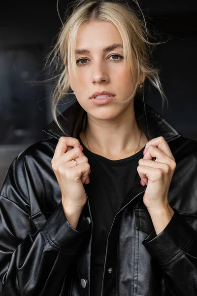Portrait of young blonde woman adjusting collar of leather shirt jacket — Stock Photo