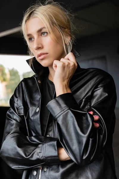 Portrait of blonde woman adjusting collar of leather shirt jacket — Stock Photo