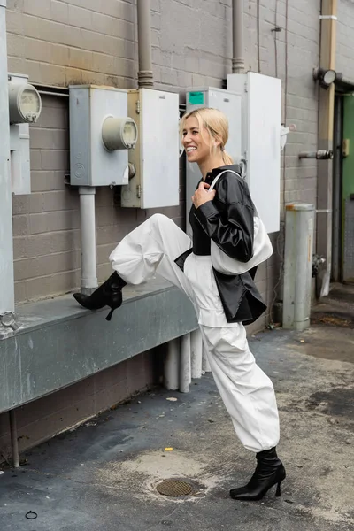 Повно веселої жінки в шкіряній сорочці і вантажних штанях з сумочкою на промисловій вулиці в Маямі. — стокове фото