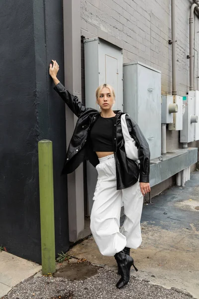 Blonde Frau in Lederjacke und Cargohose steht mit Handtasche auf Industriestraße in Miami — Stockfoto